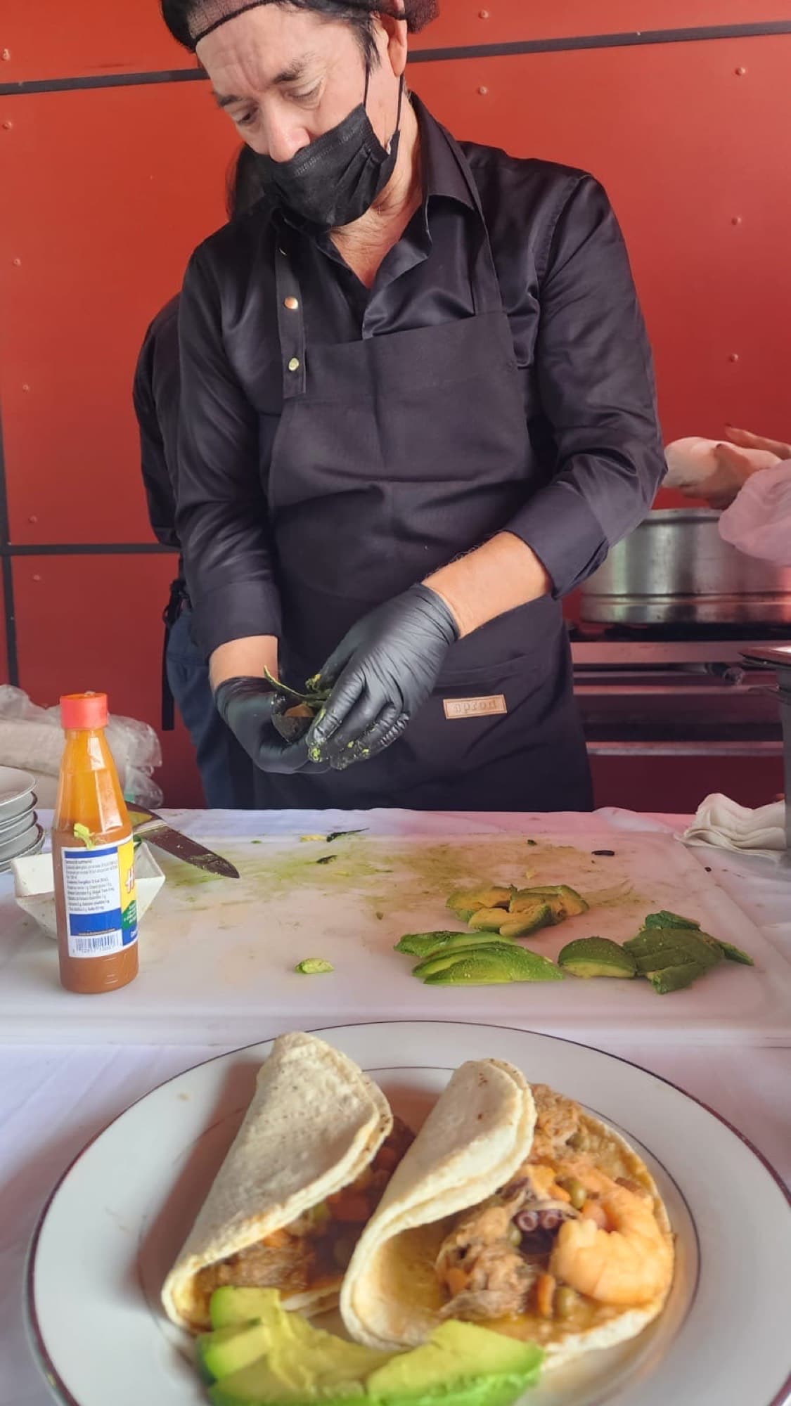 Cocinero con cubrebocas y guantes emplatando tacos de mariscos